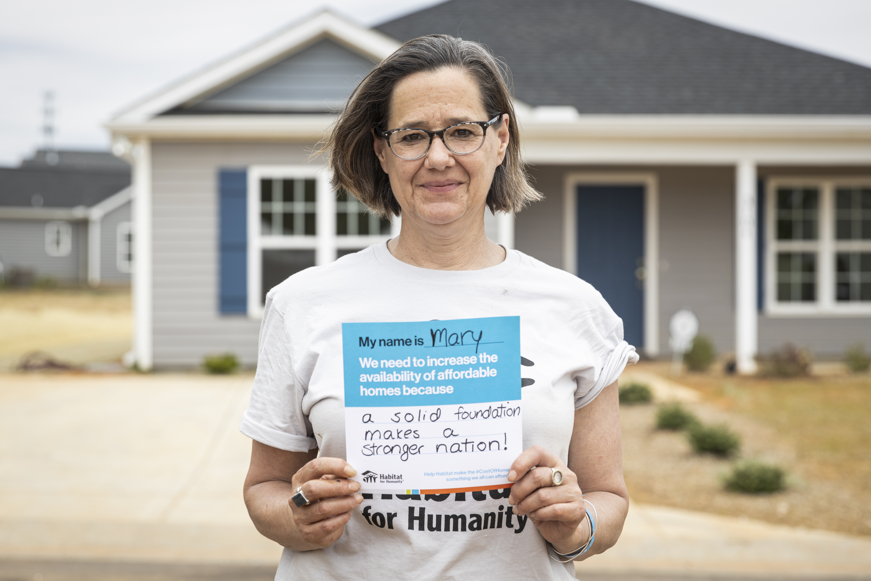 A lady holding a sign that says "My name is Mary, and we need to increase the availability of affordable homes because a solid foundation makes a stronger nation" 