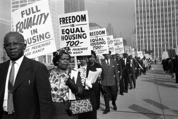 Black and white photo of Black people marching with signs for housing equality