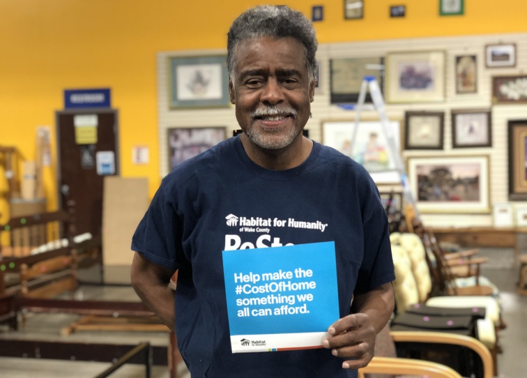 A man holding a card that says that the cost of home should not be more than a family can afford