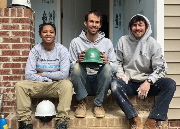 Three Habitat Wake Americorps Members sitting in the steps of a house.